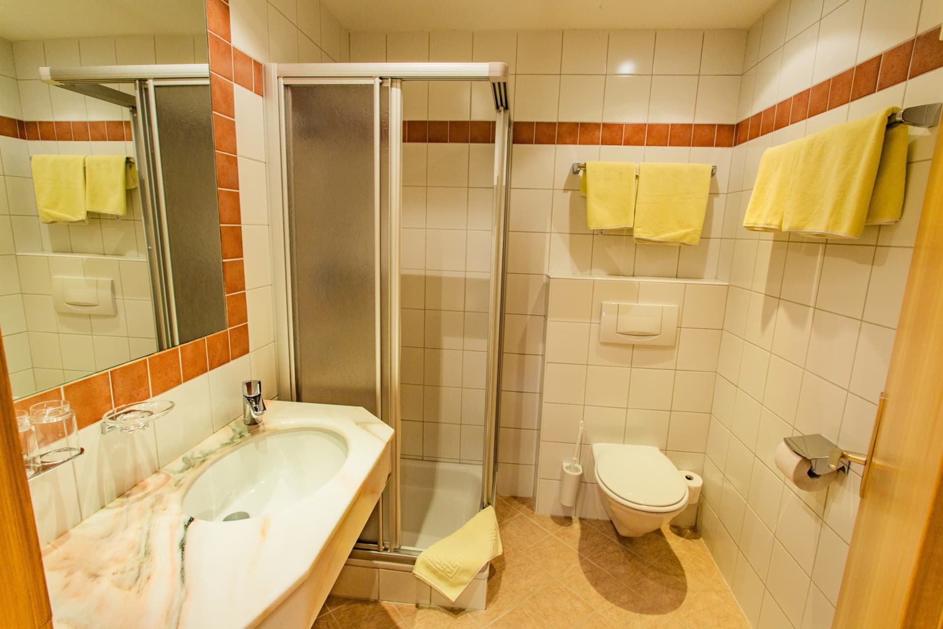 Dusche und Badezimmer im Hotel Pehab mit hellen Fliesen und Handtüchern.