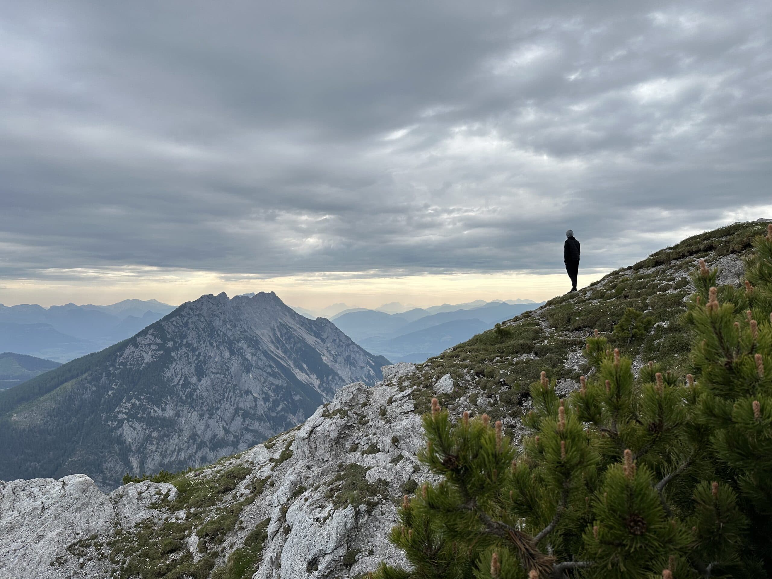 Person steht auf einem felsigen Bergrücken und blickt über das Dachstein-Gebiet.