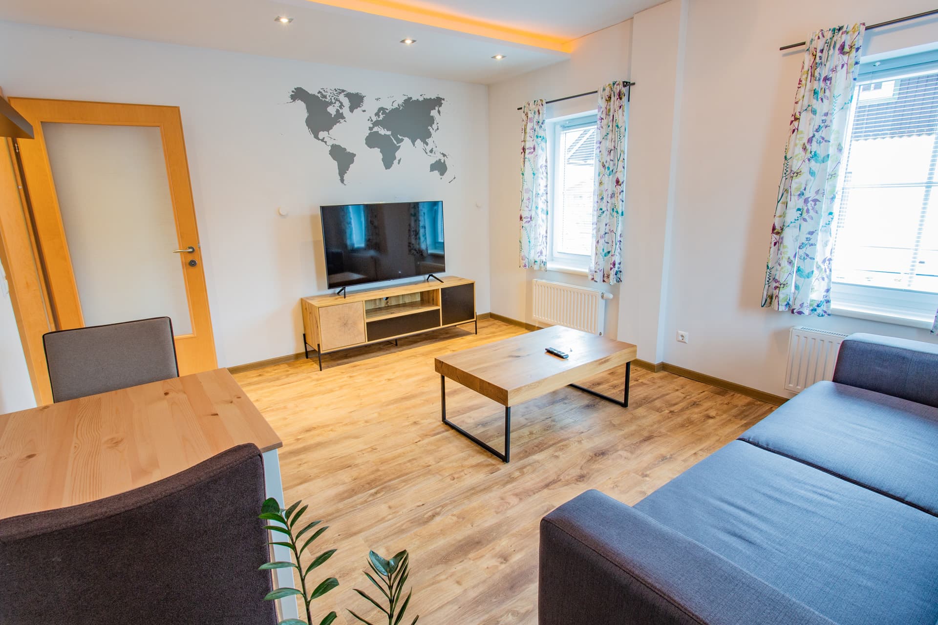 Wohnbereich mit Sofa, TV und Weltkartenbild im Appartement des Hotel Pehab.