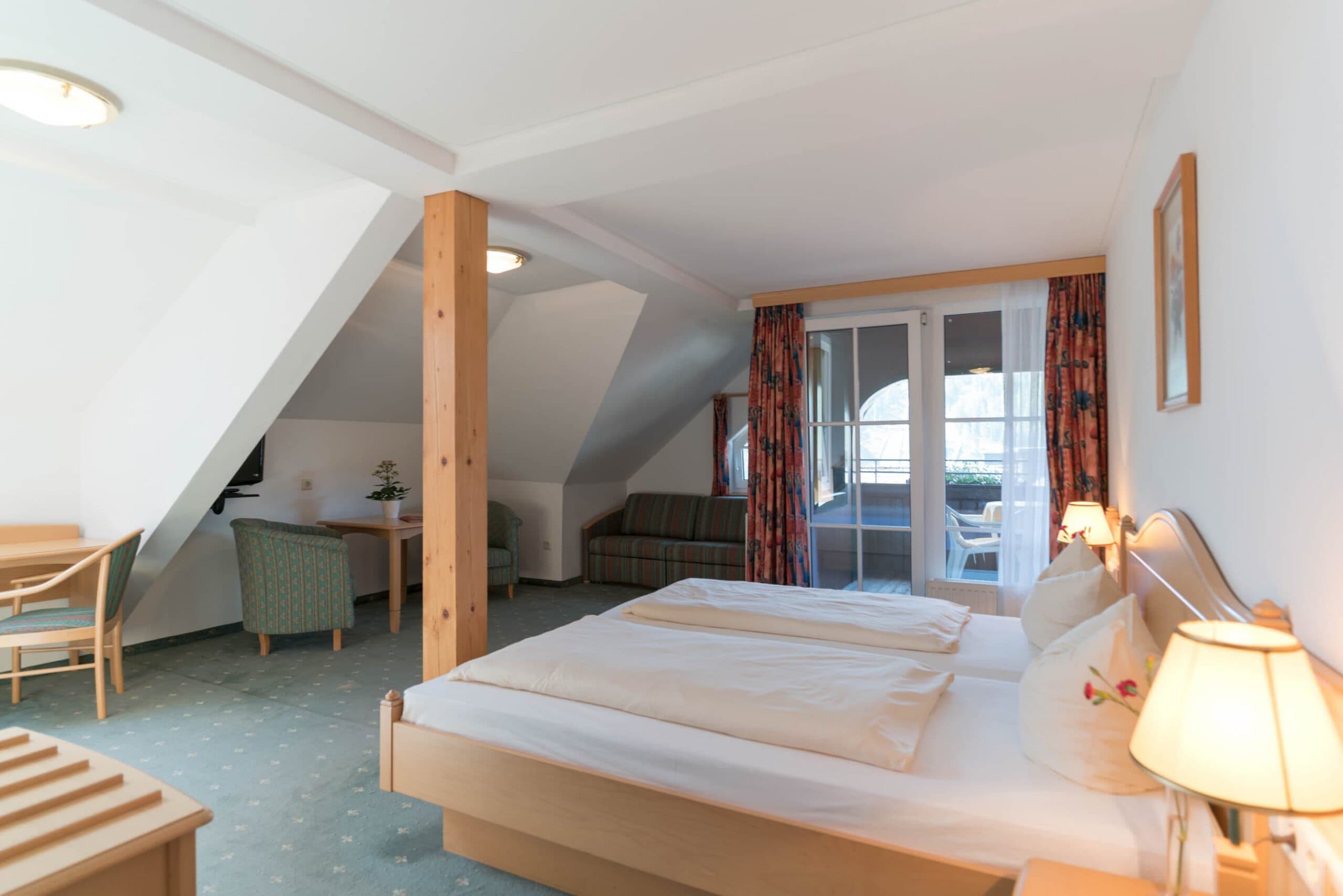 Doppelzimmer mit Blumen-Dekoration und Dachschräge im Hotel Pehab. Großes Doppelzimmer mit Sitzbereich und Balkonzugang im Hotel Pehab.