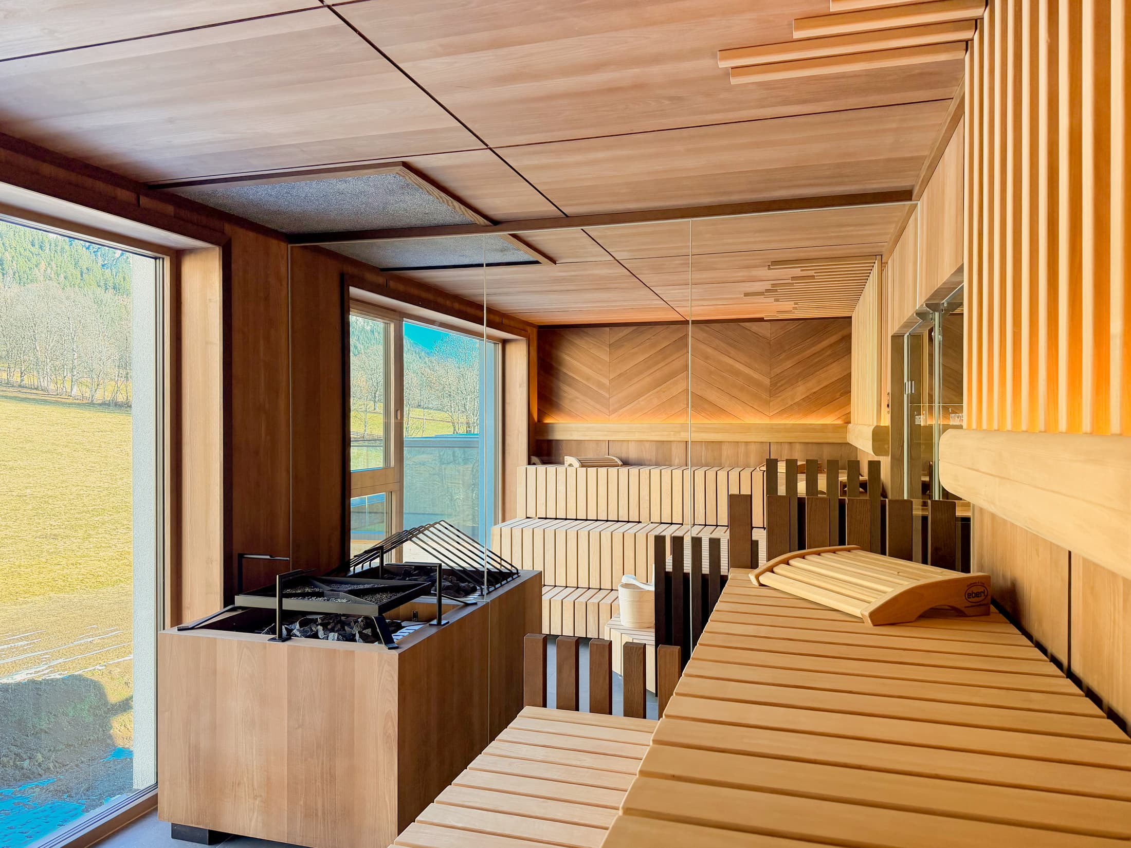 Finnische Sauna mit Holzliegen, Saunaofen und Panoramafenster mit Blick ins Grüne