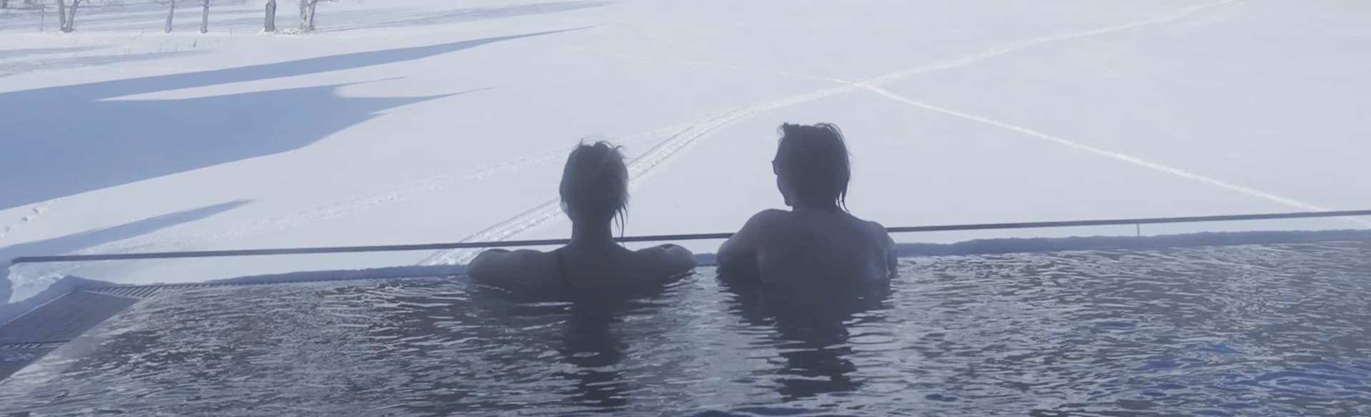 Zwei Personen im Infinity-Außenpool mit Blick auf verschneite Wiesen und Berge